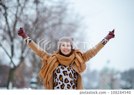 smiling modern woman in brown hat and scarf rejoicing smiling modern woman in brown hat and scarf rejoicing 108284540