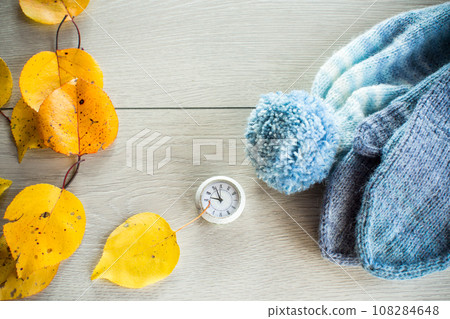 Autumn foliage, winter mittens and a clock on a wooden table. Autumn foliage, winter mittens and a clock on a wooden table. 108284648