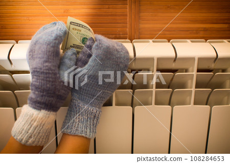 Hands in warm knitted mittens warm themselves on the radiator. 108284653