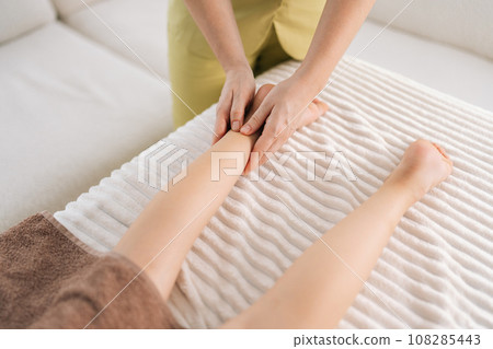 Close-up cropped shot of unrecognizable female masseur doing orthopedic leg exercises of teenager girl client, prevention of pain in foot, lying on massage table in spa salon. Concept of childcare. 108285443