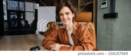 Portrait of female employee working in office, businesswoman in casual clothes writing, making notes in documents, sitting in conference room, having a meeting 108287069