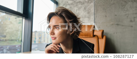 Profile shot of confident businesswoman thinking, pondering and looking outside window, thinking of something at work Profile shot of confident businesswoman thinking, pondering and looking outside window, thinking of something at work 108287127
