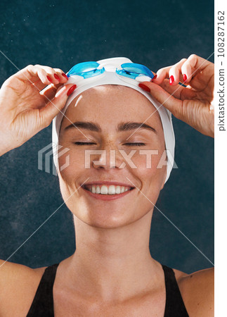 Close-up of young female swimmer standing with closed eyes adjusting goggles Close-up of young female swimmer standing with closed eyes adjusting goggles 108287162