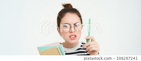 Portrait of angry woman in glasses, teacher scolding someone, shaking pen and arguing, holding notebooks, standing over white background Portrait of angry woman in glasses, teacher scolding someone, shaking pen and arguing, holding notebooks, standing over white background 108287241