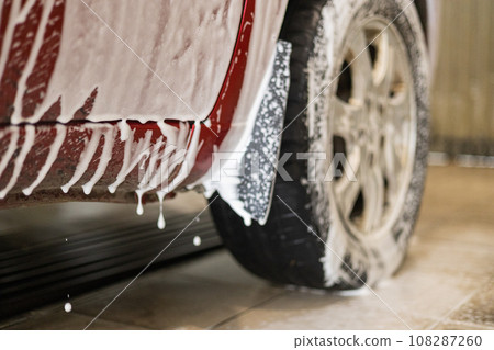 At the sink, the foam flows down and drips from the car onto the floor of the box. The car was driven to the sink to clean the dirt and dust after the road. The concept of contactless car wash. At the sink, the foam flows down and drips from the car onto the floor of the box. The car was driven to the sink to clean the dirt and dust after the road. The concept of contactless car wash. 108287260