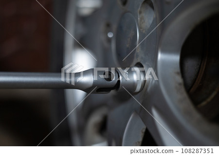 Close-up of a wrench unscrewing bolts on a wheel in a garage. A man is repairing his car in the evening in the garage. A man changes a tire on a car in a garage. 108287351