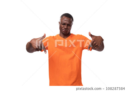 young african guy dressed in an orange t-shirt points with fingers on a white background with copy 108287384