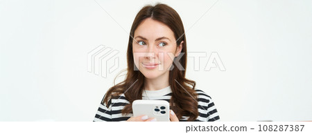 Portrait of girl with phone, woman holding smartphone and thinking, smiling and looking aside, deciding to buy smth online, white background 108287387
