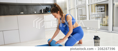Image of fitness girl, preparing her living room for workout training, unwrapping yoga mat for exercises 108287396