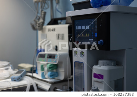The gas anesthesia machine stands in a clean light surgery ready for operation. A ventilator ready for use in an empty operating room. Anesthesia equipment concept. The gas anesthesia machine stands in a clean light surgery ready for operation. A ventilator ready for use in an empty operating room. Anesthesia equipment concept. 108287398