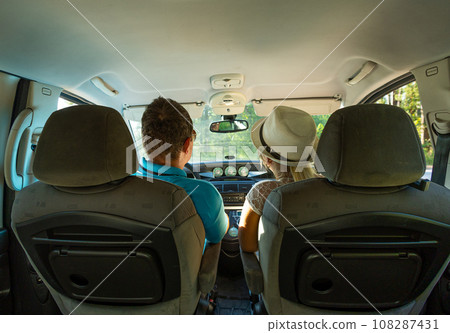 A cute young couple of travelers leaves by car. View from the salon. Husband and wife travel by car around the country. Vacation concept in auto travel. A cute young couple of travelers leaves by car. View from the salon. Husband and wife travel by car around the country. Vacation concept in auto travel. 108287431