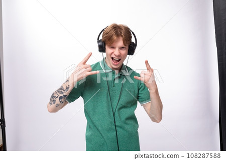 modern stylish energetic young red-haired guy in a green t-shirt listens to music in headphones 108287588