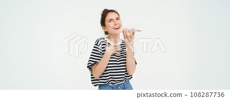 Happy young woman explaining something, using mobile phone app, talking on speakerphone, translating her voice, recording a message, holding telephone near lips, white background 108287736