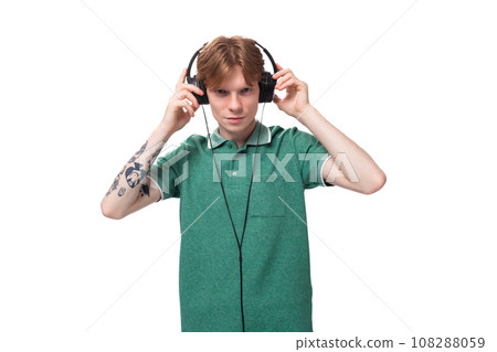 young positive slender student european man with red hair listens to music in headphones with a wire 108288059