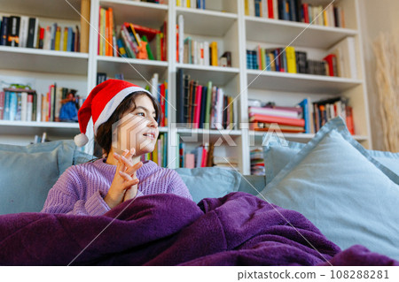sitting on sofa under warm blanket girl in santa hat watching aside sitting on sofa under warm blanket girl in santa hat watching aside 108288281
