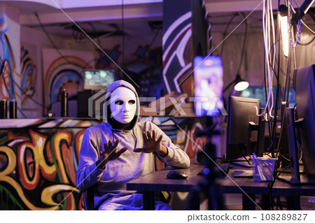 Hacker in anonymous mask live streaming illegal content online on mobile phone. Criminal recording ransom video on smartphone while planning phishing attack crime activity Hacker in anonymous mask live streaming illegal content online on mobile phone. Criminal recording ransom video on smartphone while planning phishing attack crime activity 108289827