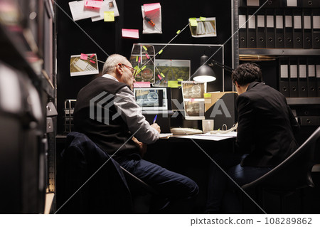Private detectives working at criminal investigations in arhive room, analyzing mysterious crime case. Senior police officer checking federal evidence while investigator writing criminology report Private detectives working at criminal investigations in arhive room, analyzing mysterious crime case. Senior police officer checking federal evidence while investigator writing criminology report 108289862