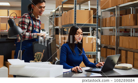 Asian team working on product inventory in warehouse, checking merchandise before shipment and distribution. Young woman doing quality control at desk, small business development. 108289884