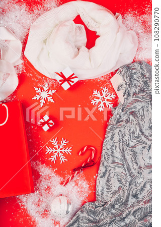 Festive Christmas attributes and decorations on a red background. Gift boxes and sequin dress on the snow. Red paper package. Festive Christmas attributes and decorations on a red background. Gift boxes and sequin dress on the snow. Red paper package. 108290770