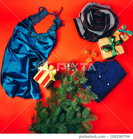 Christmas gifts on red background. Gift boxes with ribbons, branch of a Christmas tree, and clothes. Christmas gifts on red background. Gift boxes with ribbons, branch of a Christmas tree, and clothes. 108290794
