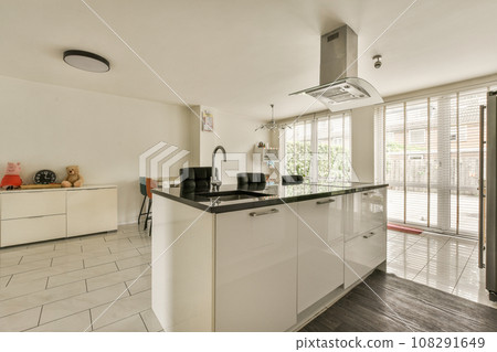 a kitchen area with white cabinets and black counter tops in the center of the image is an open door leading outside patio a kitchen area with white cabinets and black counter tops in the center of the image is an open door leading outside patio 108291649