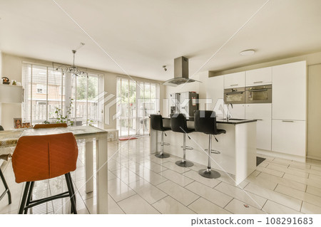 a kitchen and dining area in a house with white tiles on the floor, red bar stools and an orange chair a kitchen and dining area in a house with white tiles on the floor, red bar stools and an orange chair 108291683