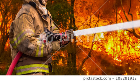 Firefighter spray water to bushfire. Tropical wildfires release carbon dioxide (CO2) emissions that contribute to climate change and global warming. 108291912