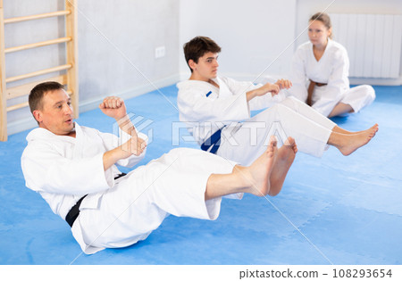 Woman and men in kimono train abdominal muscles and do punches at same time during karate or judo training 108293654