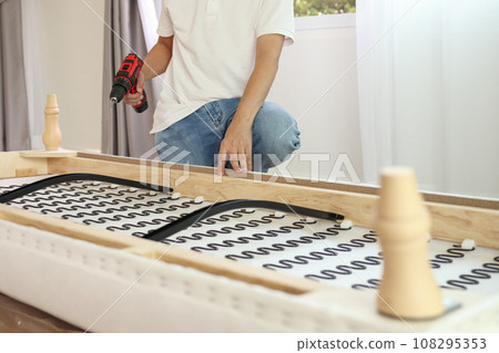 man assembling sofa furniture at home using cordless screwdriver 108295353