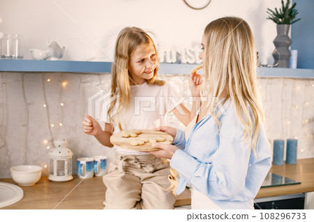 Family preparation of ginger biscuits with daughter. Mother and little girl trying a cookies. Blonde woman wearing blue shirt and girl white t-shirt. Family preparation of ginger biscuits with daughter. Mother and little girl trying a cookies. Blonde woman wearing blue shirt and girl white t-shirt. 108296733