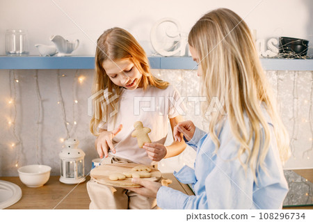 Family preparation of ginger biscuits with daughter. Mother and little girl trying a cookies. Blonde woman wearing blue shirt and girl white t-shirt. Family preparation of ginger biscuits with daughter. Mother and little girl trying a cookies. Blonde woman wearing blue shirt and girl white t-shirt. 108296734