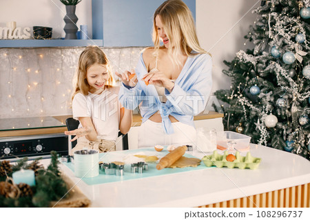 Family preparation of ginger biscuits with daughter. Mother and little girl break an egg. Blonde woman wearing blue shirt and girl white t-shirt. 108296737