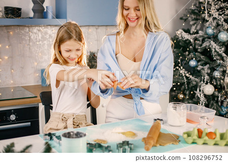 Family preparation of ginger biscuits with daughter. Mother and little girl break an egg. Blonde woman wearing blue shirt and girl white t-shirt. Family preparation of ginger biscuits with daughter. Mother and little girl break an egg. Blonde woman wearing blue shirt and girl white t-shirt. 108296752
