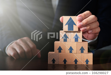 業務成長策略和成功成就的形象。一名男子將木塊堆放在桌上。箭頭圖示和 108298027