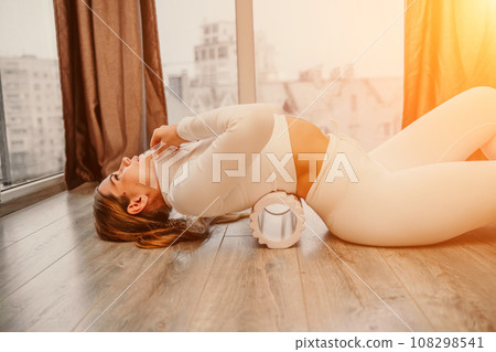 Adult athletic woman, in white bodysuit, performing fascia exercises on the floor - caucasian woman using a massage foam roller - a tool to relieve tension in the back and relieve muscle pain - the 108298541