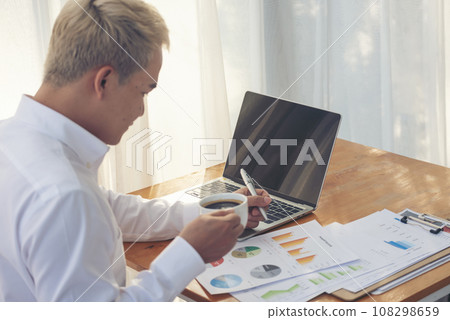 Asian man freelance using laptop at home office desk. man reading financial graph chart Planning analyzing computer data. Asian male people working office business stuff, coffee cup at home office 108298659