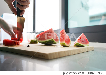 woman hand use knife slice of watermelon on wood board in kitchen woman hand use knife slice of watermelon on wood board in kitchen 108298936