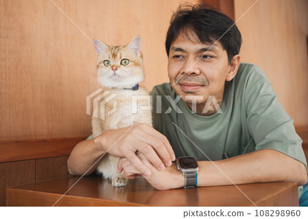 asian man smile and happy during play with his gold british cat in coffee shop asian man smile and happy during play with his gold british cat in coffee shop 108298960