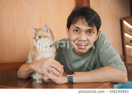 asian man smile and happy during play with his gold british cat in coffee shop asian man smile and happy during play with his gold british cat in coffee shop 108298961