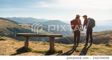 Couple of Hikers With Backpacks in Front of Landscape Valley View on Top of a Mountain 108299096