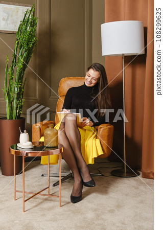 Beautiful smiling woman sitting in armchair and writing notes 108299625