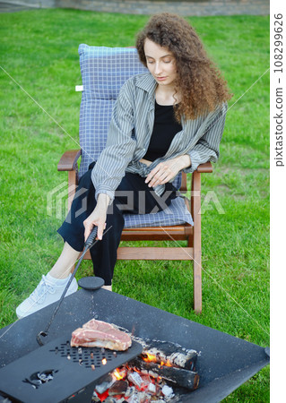 Woman stirs the coals while cooking a steak on the grill Woman stirs the coals while cooking a steak on the grill 108299626