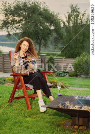 Woman eat grilled meat near fireplace in her country house Woman eat grilled meat near fireplace in her country house 108299629