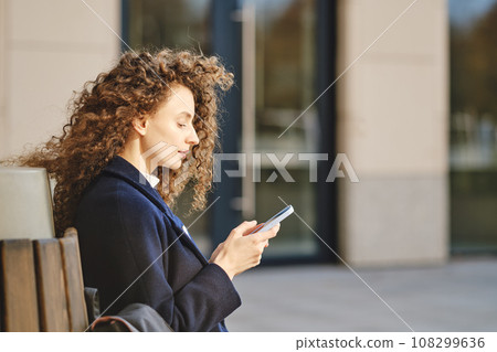 Young woman sits on bench and scrolling through social network 108299636