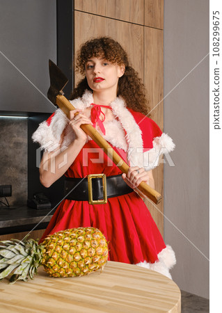 Young woman in christmas masquerade dress holds axe on her shoulder Young woman in christmas masquerade dress holds axe on her shoulder 108299675