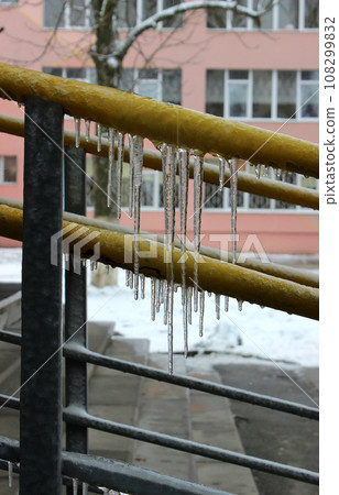 Icicles hang from the iron railing of the main entrance to a multi-storey building Icicles hang from the iron railing of the main entrance to a multi-storey building 108299832