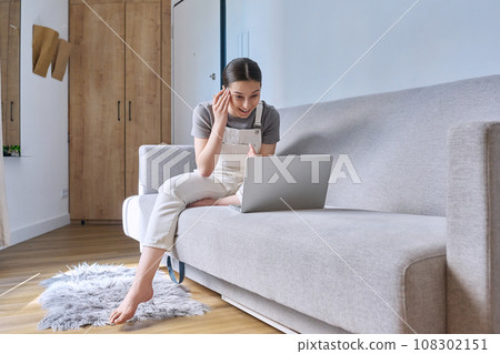 Teen girl at home on couch using laptop, emotional talking Teen girl at home on couch using laptop, emotional talking 108302151