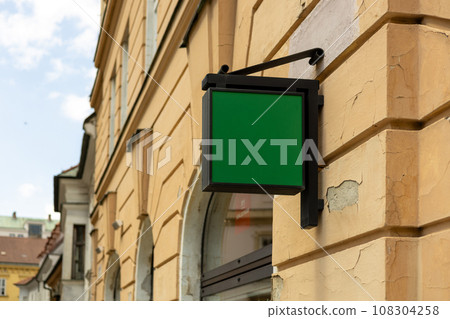 Blank sign mockup in the urban environment. Green rectangle sign with blank space for cafe or restaurant name and logo, in an old town 108304258