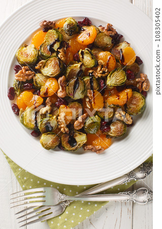 Delicious warm Brussels sprouts salad with tangerines, walnuts and dried cranberries dressed with balsamic glaze close-up in a plate on the table. Vertical top view Delicious warm Brussels sprouts salad with tangerines, walnuts and dried cranberries dressed with balsamic glaze close-up in a plate on the table. Vertical top view 108305402