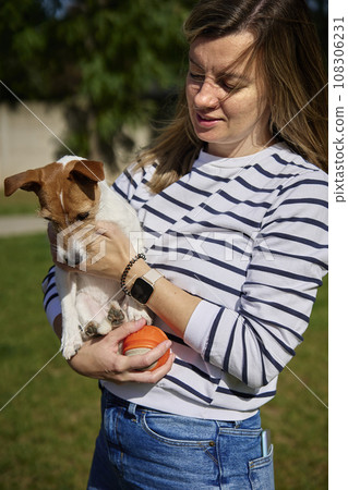 Woman holds her dog on hands and embracing with it. Happy female owner hugging and kissing cute friend. Pet care Woman holds her dog on hands and embracing with it. Happy female owner hugging and kissing cute friend. Pet care 108306231